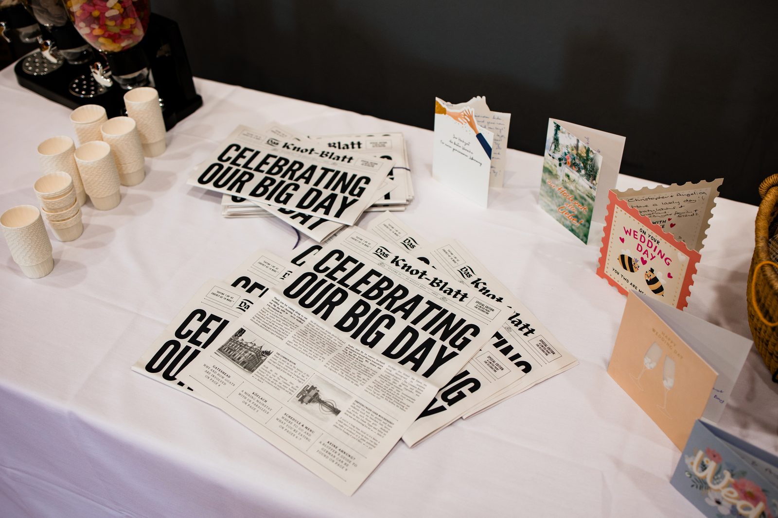 A stack of printed wedding newspapers on the welcome table beside the cards