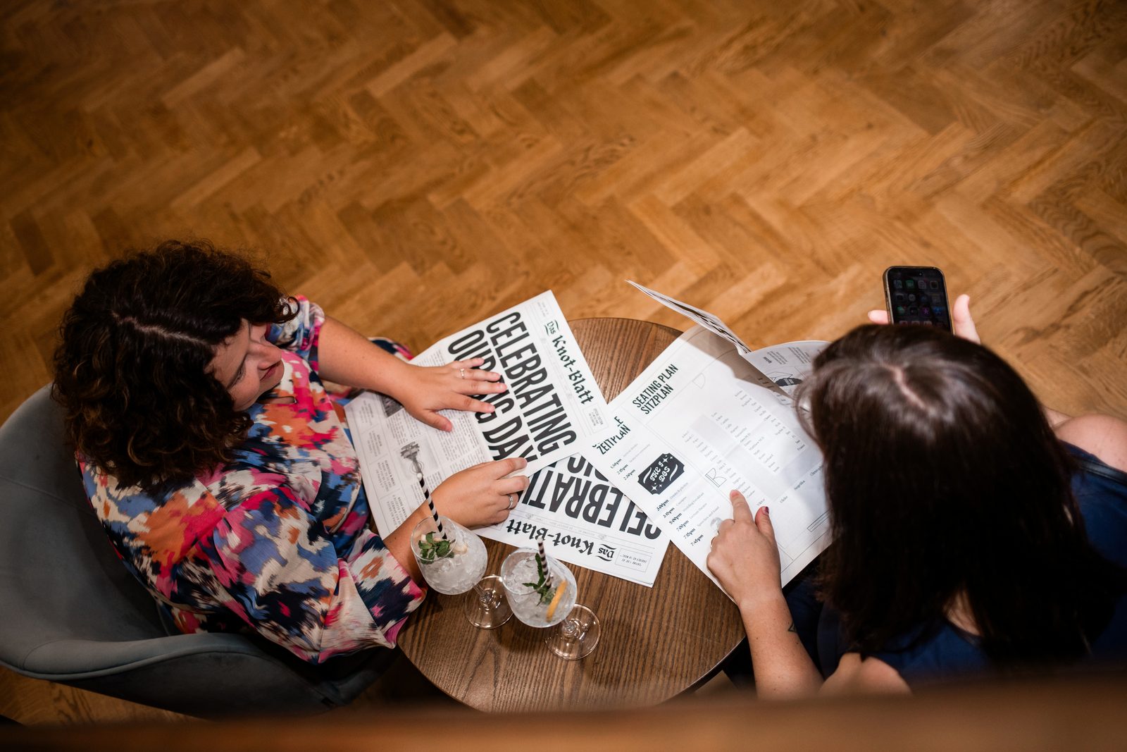 Two wedding guests at a small round table reading the newspaper, seen from above